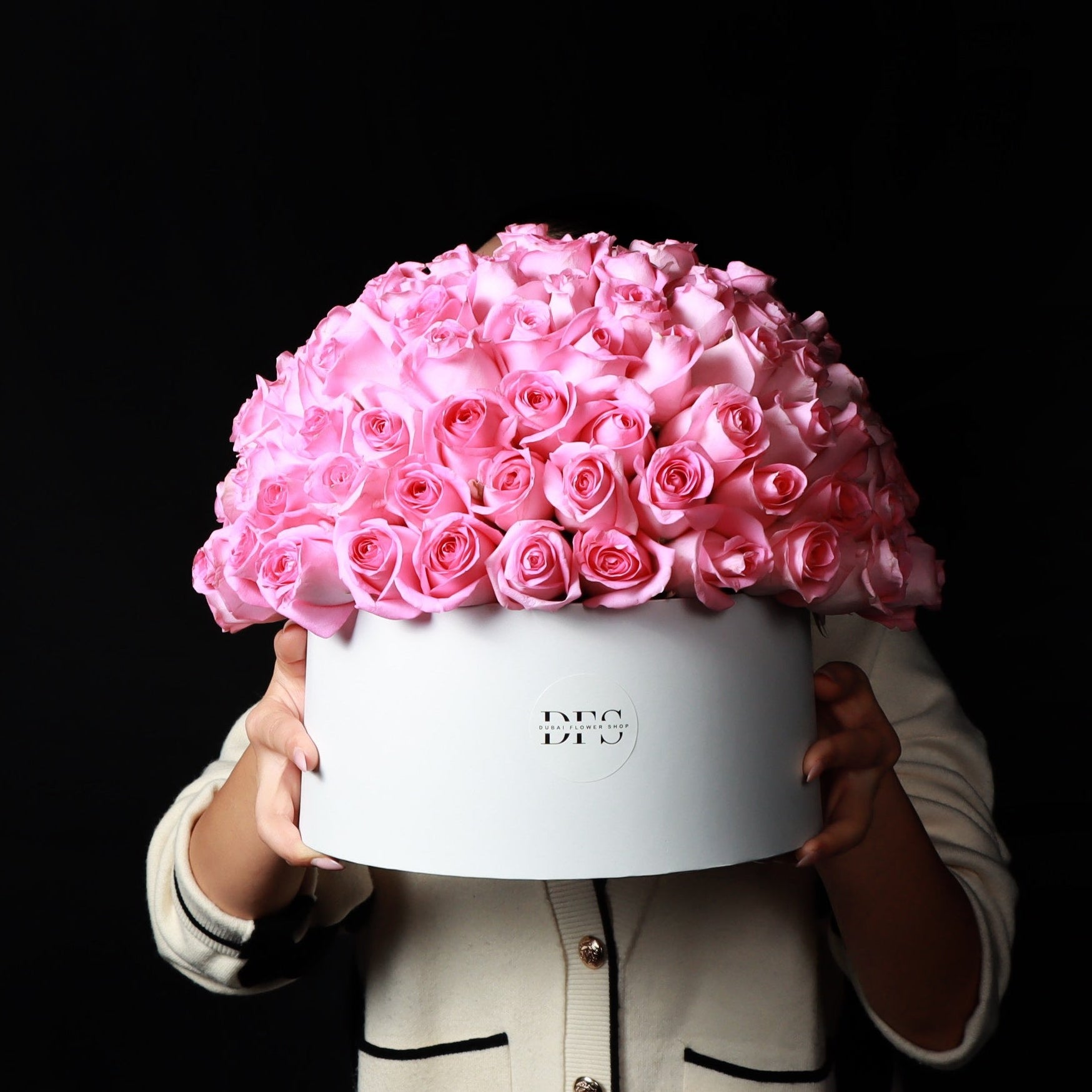 Person holding a large white box filled with pink roses against a black background Main image